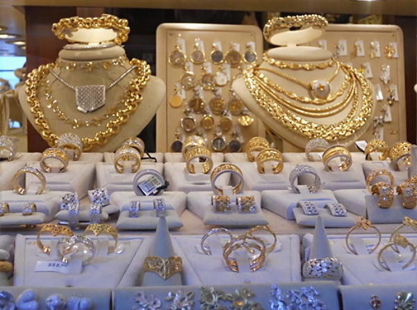 Shop display of gold necklaces and rings on white stands — upscaled by GoStudio Lite