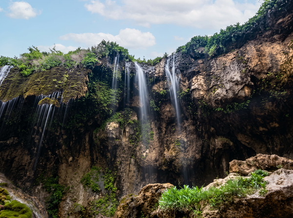 Waterfall over a dark rock face into a gorge with green vegetation — upscaled by GoStudio Advanced
