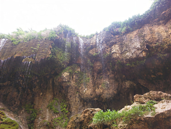 Waterfall over a dark rock face into a gorge with green vegetation — upscaled by GoStudio Pro