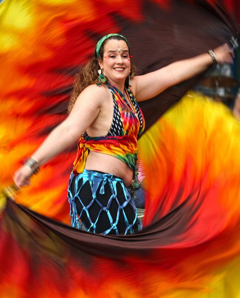 Festival dancer with an arm raised, swirling red and orange fans behind her — upscaled by GoStudio Advanced