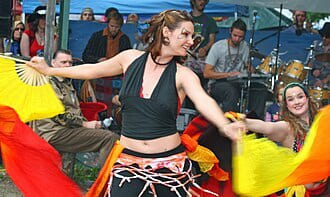 Woman in a black halter top dancing with yellow fans in front of a seated crowd
