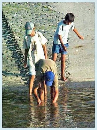 Three boys paddling in shallow water at the foot of a stone slipway