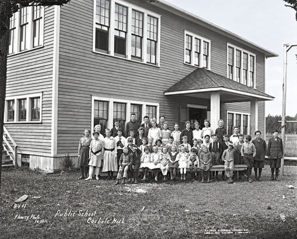 Black-and-white school photograph of pupils lined up in front of a two-storey clapboard school — upscaled by GPT Image 2.5