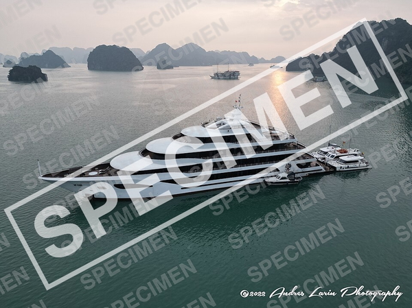 Aerial view of a white superyacht moored among limestone karsts at dusk