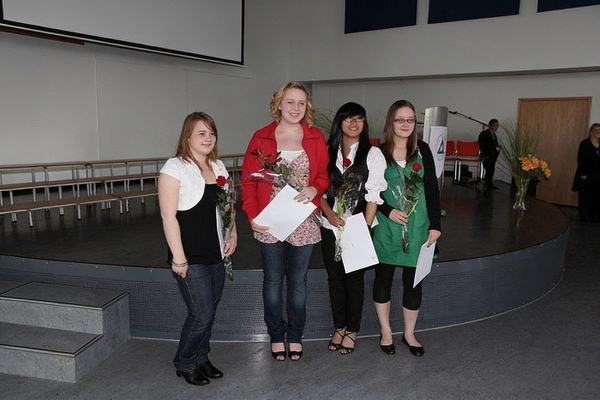 Four graduates holding certificates and flowers on a hall stage — watermark removed by GoStudio Advanced
