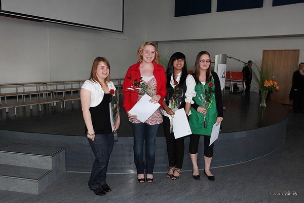 Four graduates holding certificates and flowers on a hall stage — watermark removed by GoStudio Lite