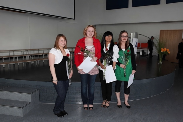 Four graduates holding certificates and flowers on a hall stage — watermark removed by GoStudio Pro