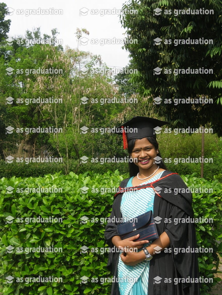 Graduate in a black gown and cap over a pale blue dress, in front of a hedge