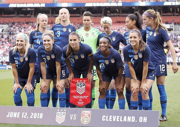 Women’s football team in navy kit lined up before a match, with a match-day banner — watermark removed by GoStudio Lite