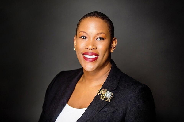 Woman in a navy blazer with an elephant brooch, smiling, on a dark backdrop — watermark removed by GoStudio Lite