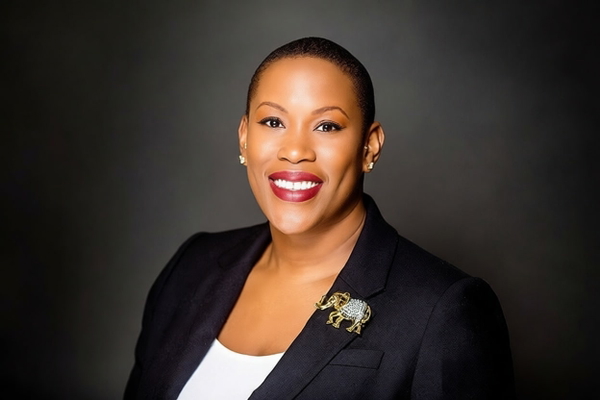 Woman in a navy blazer with an elephant brooch, smiling, on a dark backdrop — watermark removed by GoStudio Pro
