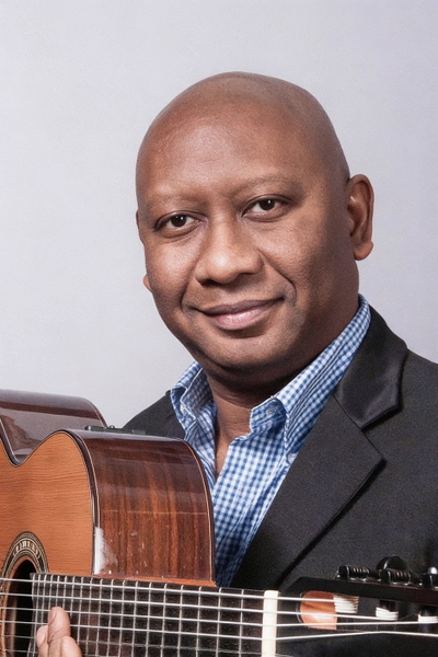 Smiling man in a checked shirt and dark jacket holding a guitar — watermark removed by GoStudio Advanced