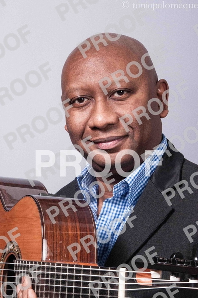Smiling man in a checked shirt and dark jacket holding a guitar