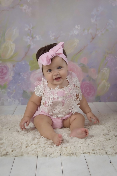 Baby in a pink bow sitting on a fluffy rug against a floral backdrop — watermark removed by GoStudio Advanced