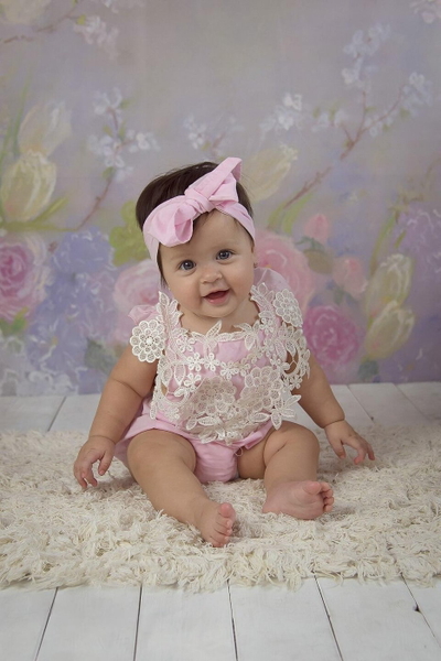 Baby in a pink bow sitting on a fluffy rug against a floral backdrop — watermark removed by GoStudio Lite