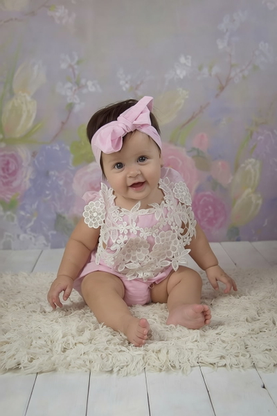 Baby in a pink bow sitting on a fluffy rug against a floral backdrop — watermark removed by GoStudio Pro