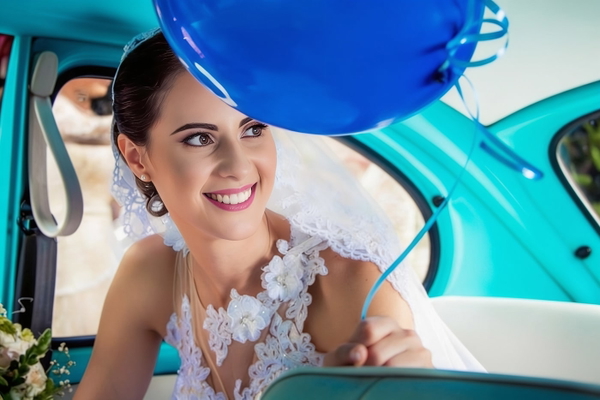 Smiling bride in a lace veil in a turquoise vintage car, blue balloons above — watermark removed by GoStudio Advanced