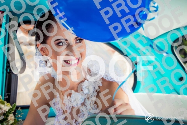 Smiling bride in a lace veil in a turquoise vintage car, blue balloons above