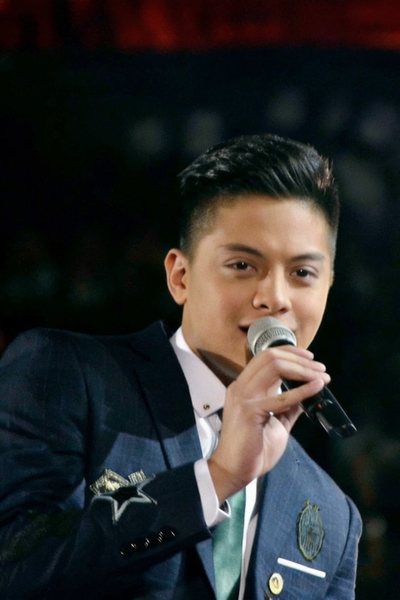 Young man in a blue suit singing into a microphone on a dark stage — watermark removed by GoStudio Advanced