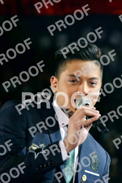 Young man in a blue suit singing into a microphone on a dark stage