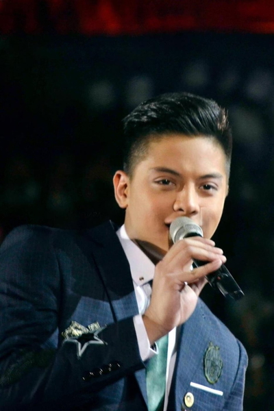 Young man in a blue suit singing into a microphone on a dark stage — watermark removed by GoStudio Lite