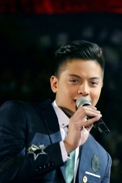 Young man in a blue suit singing into a microphone on a dark stage — watermark removed by GoStudio Pro