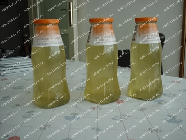 Three glass bottles of pale yellow liquid on a patterned tablecloth