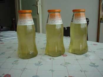 Three glass bottles of pale yellow liquid on a patterned tablecloth — watermark removed by GoStudio Lite