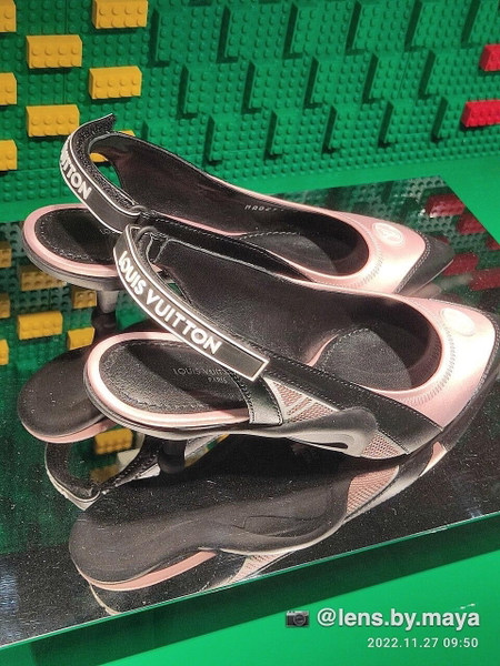Pair of branded slingback shoes on a mirrored stand against green bricks — watermark removed by GoStudio Lite