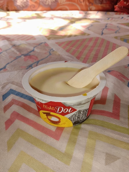 Cup of sweet yoghurt with a wooden spoon on a patterned bedspread — watermark removed by GoStudio Advanced