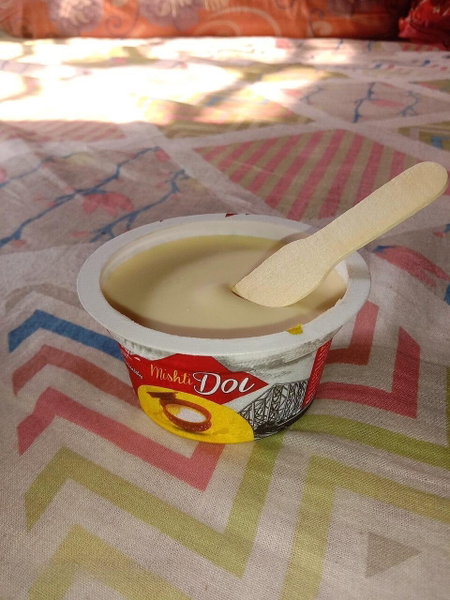 Cup of sweet yoghurt with a wooden spoon on a patterned bedspread — watermark removed by GoStudio Lite
