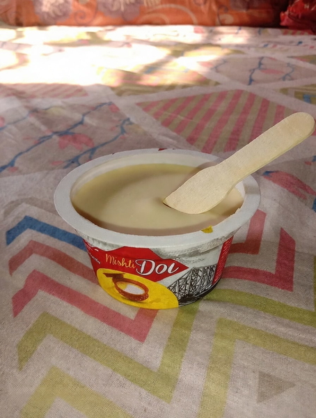 Cup of sweet yoghurt with a wooden spoon on a patterned bedspread — watermark removed by GoStudio Pro