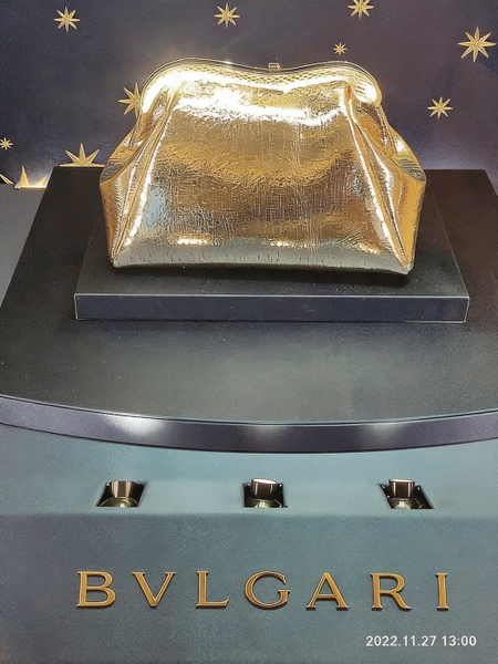 Gold clutch bag on a display plinth above a jeweller’s name — watermark removed by GoStudio Advanced