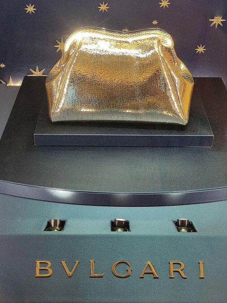 Gold clutch bag on a display plinth above a jeweller’s name — watermark removed by GoStudio Lite