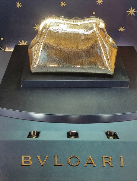 Gold clutch bag on a display plinth above a jeweller’s name — watermark removed by GoStudio Pro