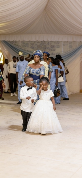 Phone screenshot of a gallery showing a child in a white suit at a wedding procession — watermark removed by GoStudio Advanced