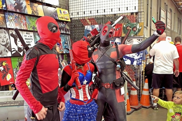 People in superhero costumes at a comic convention stall — watermark removed by GoStudio Advanced