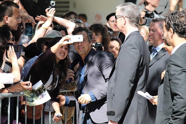 Crowd of fans with phones around a man in a grey suit at a public event — watermark removed by GoStudio Lite