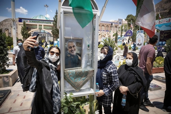 Women in masks taking selfies at an outdoor memorial with flags — watermark removed by GoStudio Advanced