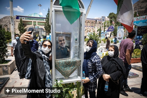 Women in masks taking selfies at an outdoor memorial with flags