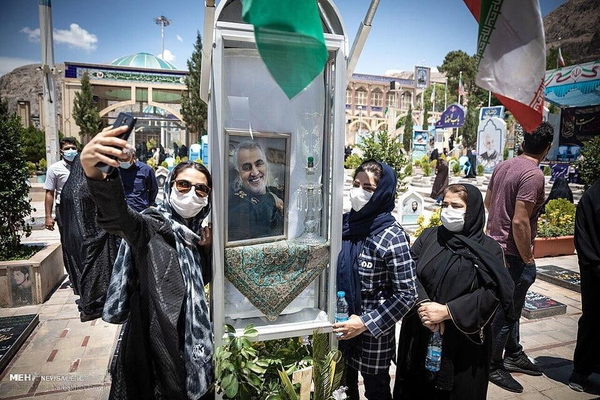 Women in masks taking selfies at an outdoor memorial with flags — watermark removed by GoStudio Lite