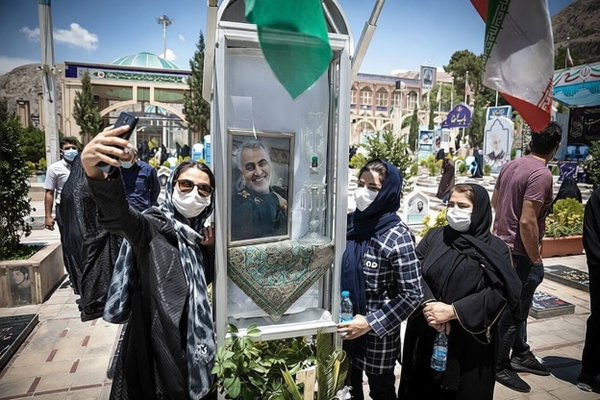 Women in masks taking selfies at an outdoor memorial with flags — watermark removed by GoStudio Pro