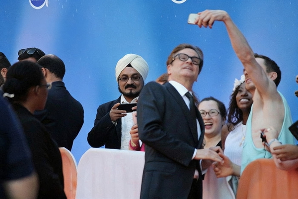 Crowd taking selfies with a man in a dark suit and glasses in front of a blue backdrop — watermark removed by GoStudio Advanced
