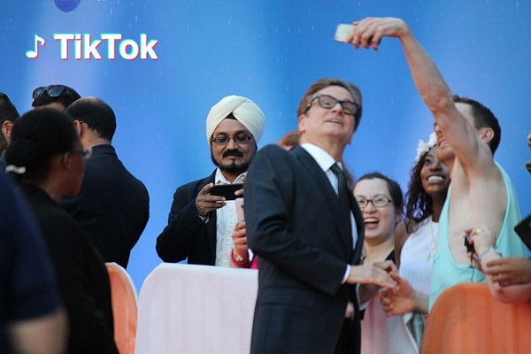 Crowd taking selfies with a man in a dark suit and glasses in front of a blue backdrop — watermark removed by GoStudio Lite