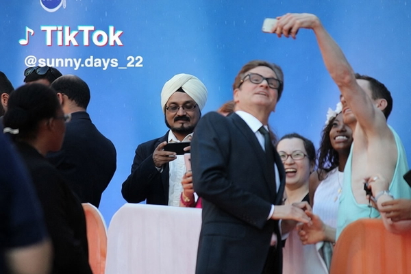 Crowd taking selfies with a man in a dark suit and glasses in front of a blue backdrop — watermark removed by GoStudio Pro