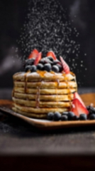 Stack of pancakes with blueberries and strawberries on top, sitting on a plate on a table — sample image to deblur