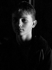 Young boy in a black shirt looking at the camera against a dark background — sample image to denoise