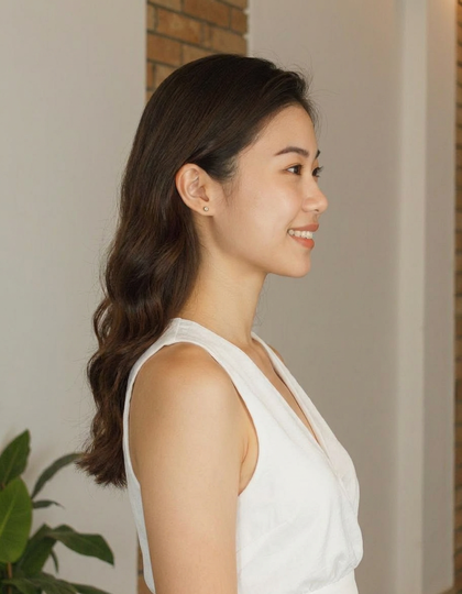 A woman in a white dress, smiling, with sleek, straight hair, standing by a plant and a brick wall, re-rendered from a right-side (90° profile) camera angle by AI.