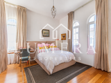A furnished bedroom with a large bed and pillows, a rug, chairs, a table and curtained windows, shown with a watermark.