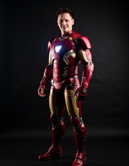 A man in a red and gold suit stands confidently, smiling, against a black background.